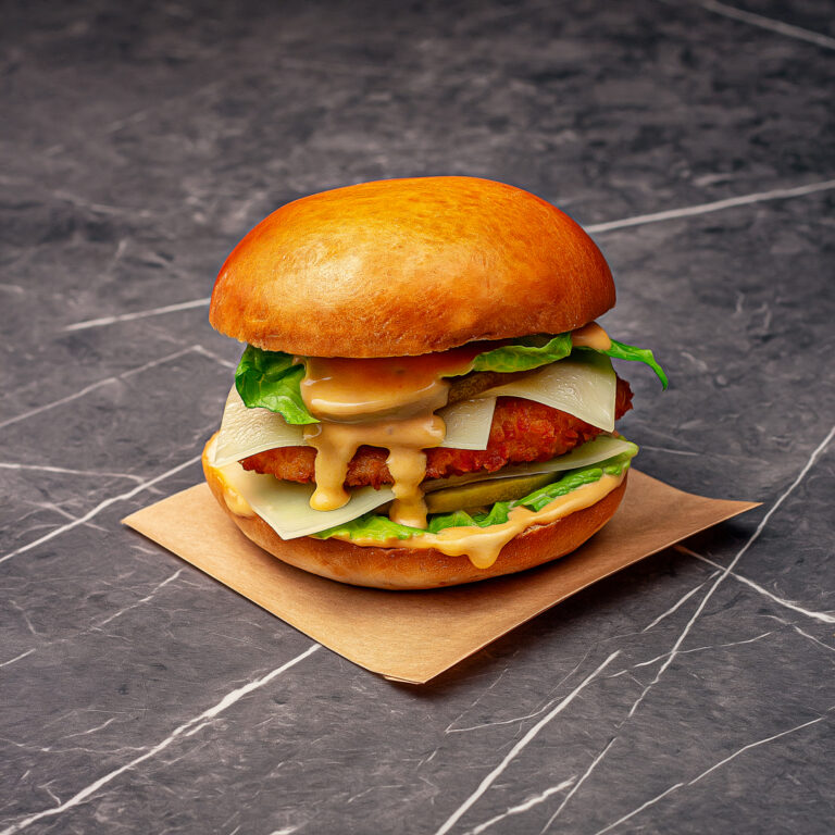 Un pain garni d'une pièce de volaille panée frite croustillante, deux tranches de cornichons, deux tranches d'emmental, de la salade et de la sauce