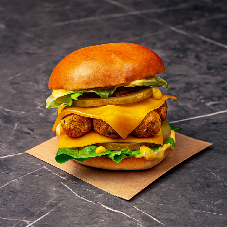 Un pain garni d'une pièce de falafels, deux tranches de cornichons, deux tranches de cheddar, de la salade et de la sauce