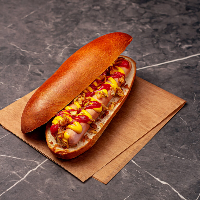 2 saucisses de volaille bio française dans un pain long, légèrement brioché, nappé de sauce moutarde douce au miel, sauce tomate aigre-douce (ketchup) le tout parsemé d’oignons frits.