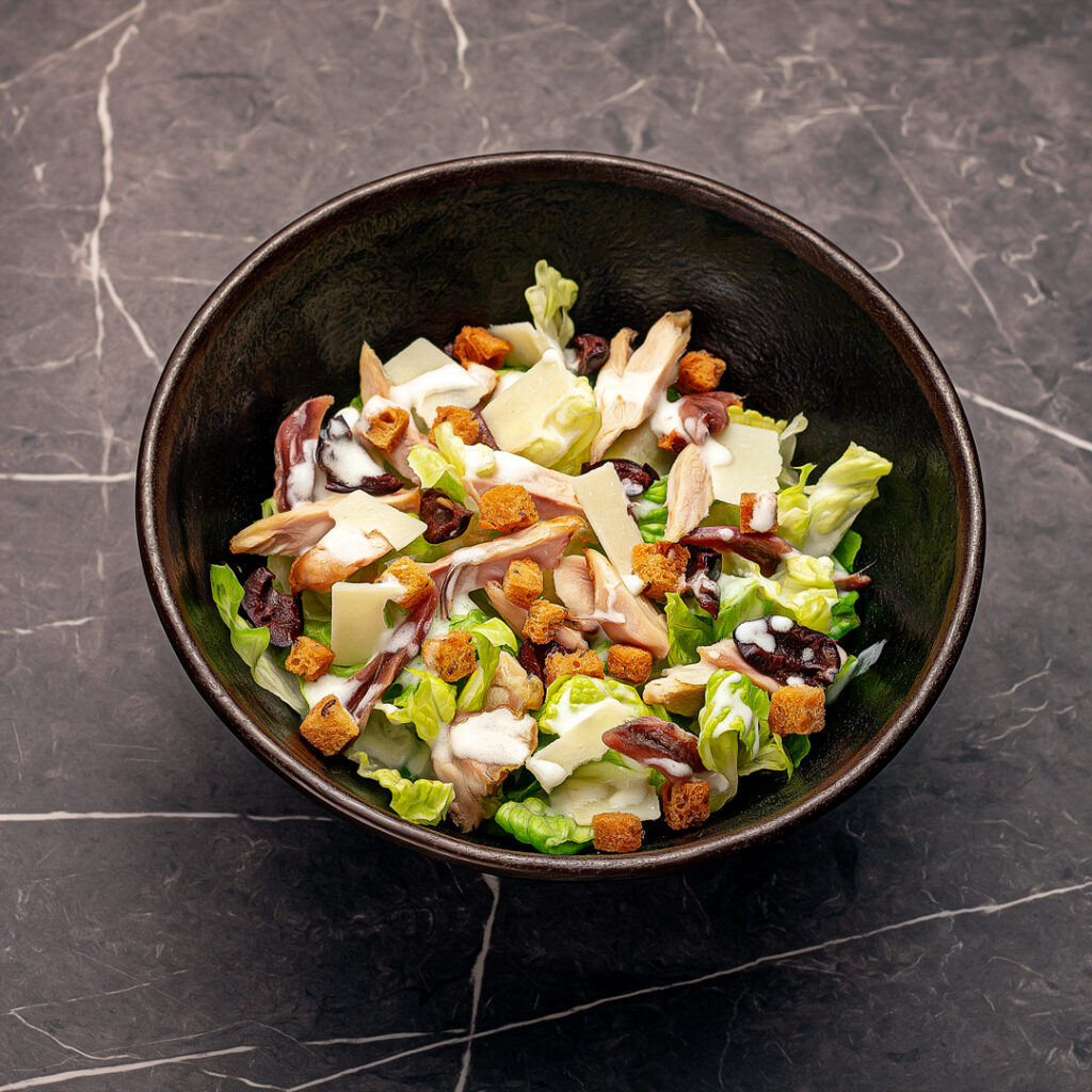 Salade complète, composée de laitue romaine finement ciselée, émincé de volaille grillé, croutons dorés, copeaux de parmesan, olive noires à la grecque, anchois et sa célèbre sauce César.