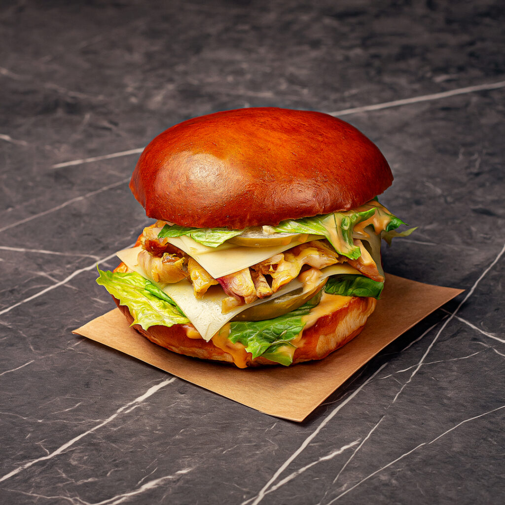 Pain garni Tom composé d'un pain rond légèrement brioché, garni d’un émincé de volaille bio et française, salade, deux tranches de Comté AOC, tranches de cornichons aigres-doux et le tout bien nappé d’une sauce à l’estragon.